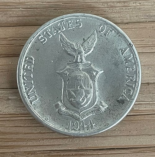 5 Centavos coin, Filipinas / United States of America, 1944. Photo: Megan E. Springate. Collection of the Author. A silver colored coin with the coat of arms of the Philippine Commonwealth with an eagle and a shield. Words circling the coat of arms read: “UNITED STATES OF AMERICA / 1944.” Collection of the Author
