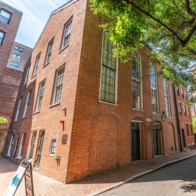 Three story red brick building with large, panned windows. 
