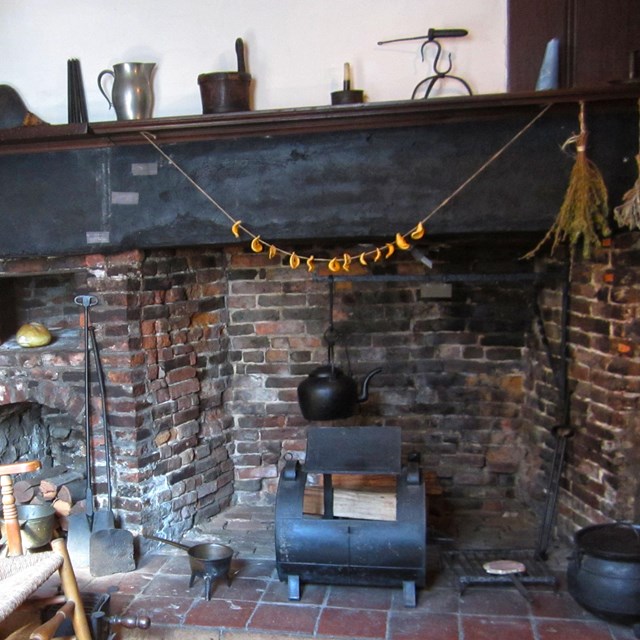A wooden chair next to a brick fireplace with a wood mantle that has cups on top.