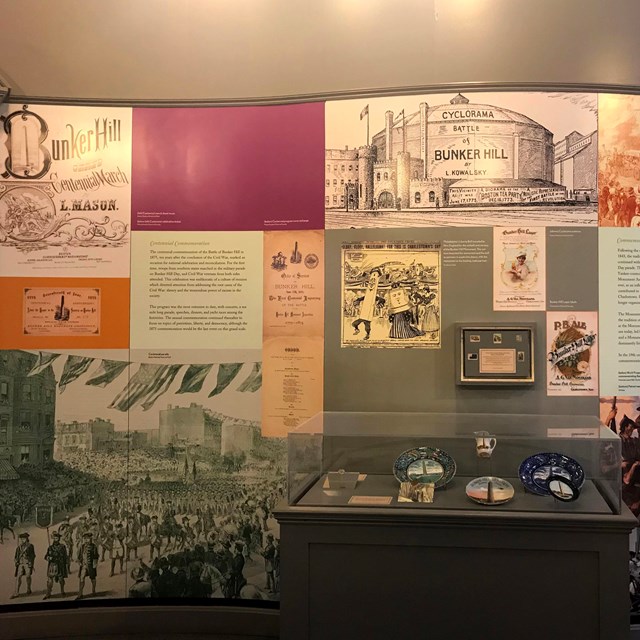 A wall of an exhibit filled with images and text. A glass case of artifacts sits in front.