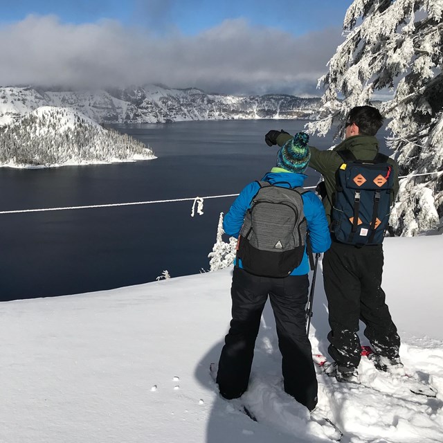 Snowshoers view the lake from behind a rope which indicates the rim edge