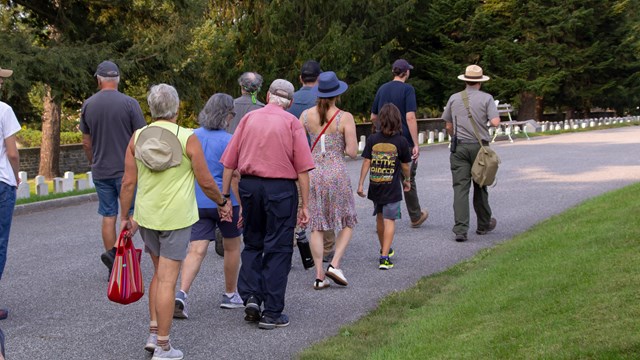 A crowd of visitors walks through Gettysburg National Cemetery with a park ranger