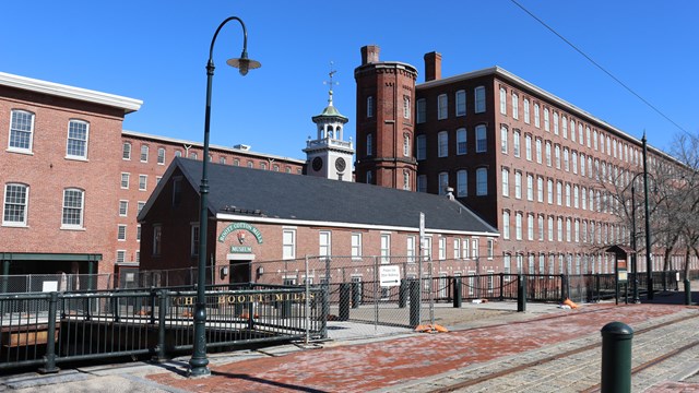 A tall brick building with many windows looms over a canalway