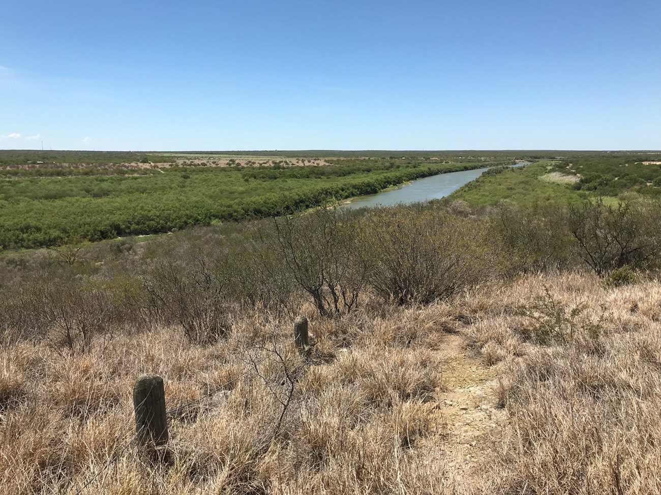 A trail leads down a grassy hillside to a river valley below.